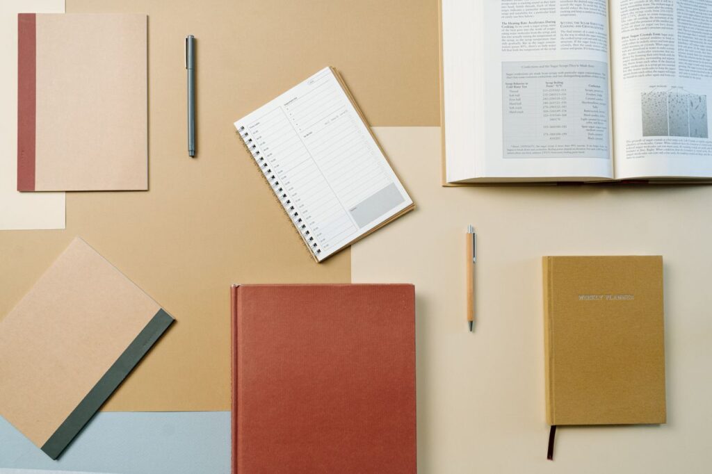 A neatly arranged flat lay of textbooks, notebooks, and stationary items on a brown background.